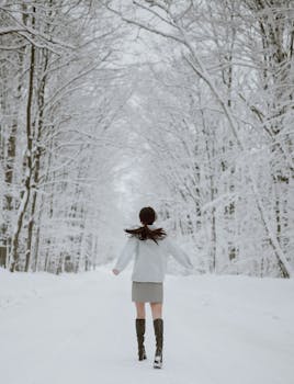 A young woman enjoys a carefree walk through a winter forest path, surrounded by snow-covered trees.