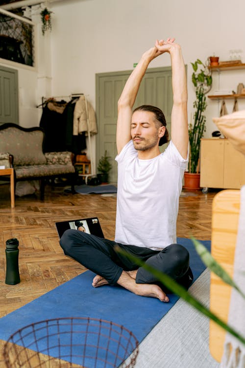 A Man in White Shirt Sitting on His Yoga Mat while Stretching His Arms