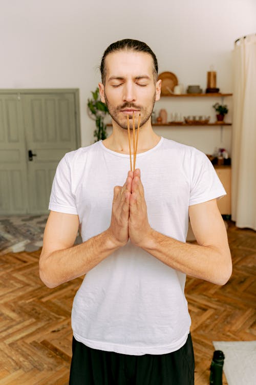 A Man in White Shirt Meditating while Holding an Incense Sticks