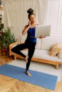 A Woman in Blue Tank Top Doing a Yoga while Holding a Laptop