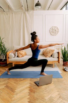 An African American woman performing the warrior pose during a yoga session indoors, focusing on wellness and fitness.
