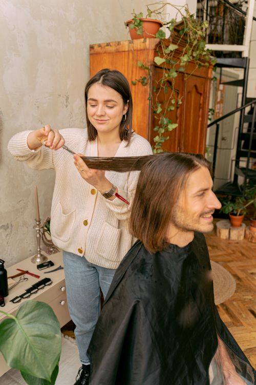 Free Woman stylist cutting a man's long hair in a cozy indoor salon setting. Stock Photo