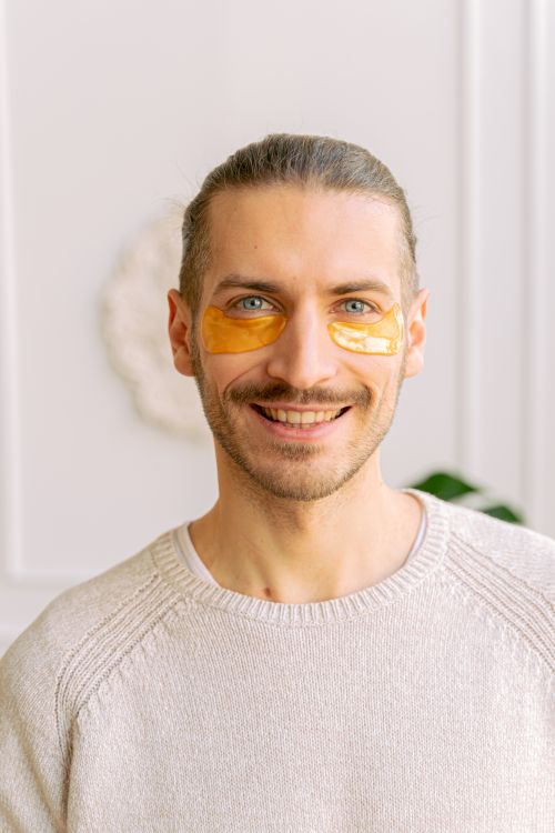 Free Portrait of a man applying under eye masks for skincare, smiling indoors. Stock Photo
