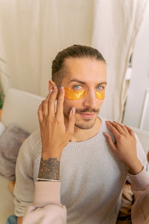 Free A Woman Applying Under Eye Masks to a Bearded Man Stock Photo