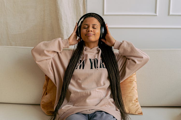 Young Woman Sitting On A Couch Listening To Music With Her Eyes Closed In Headphones