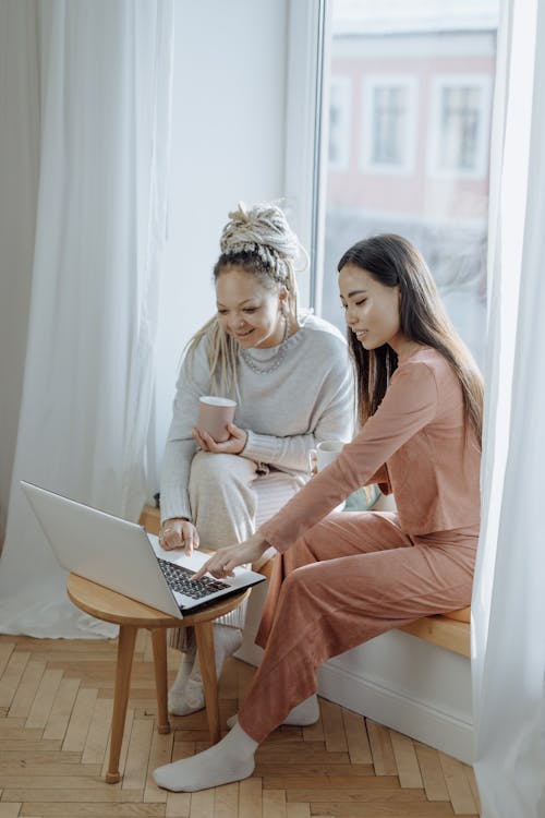 Free Women Sitting by the Window while Using Laptop Stock Photo