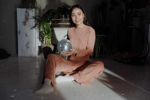 A Woman Sitting on the Floor while Holding Disco Ball