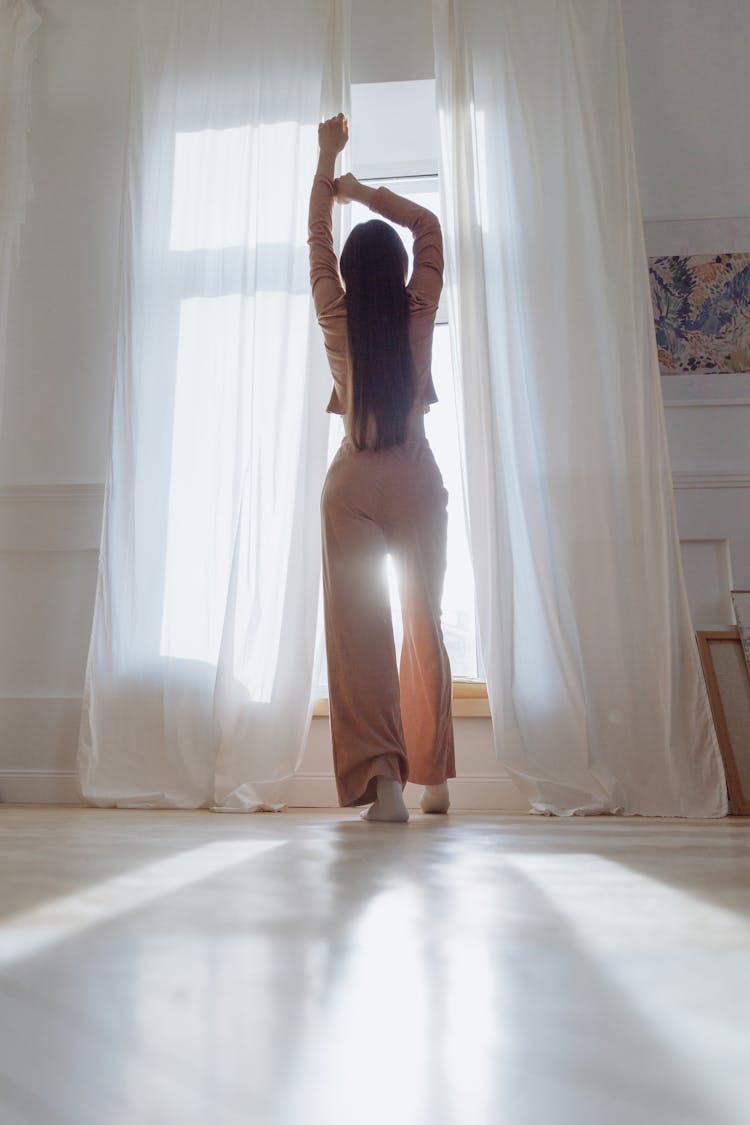 A Back View Of A Woman Standing By The Window