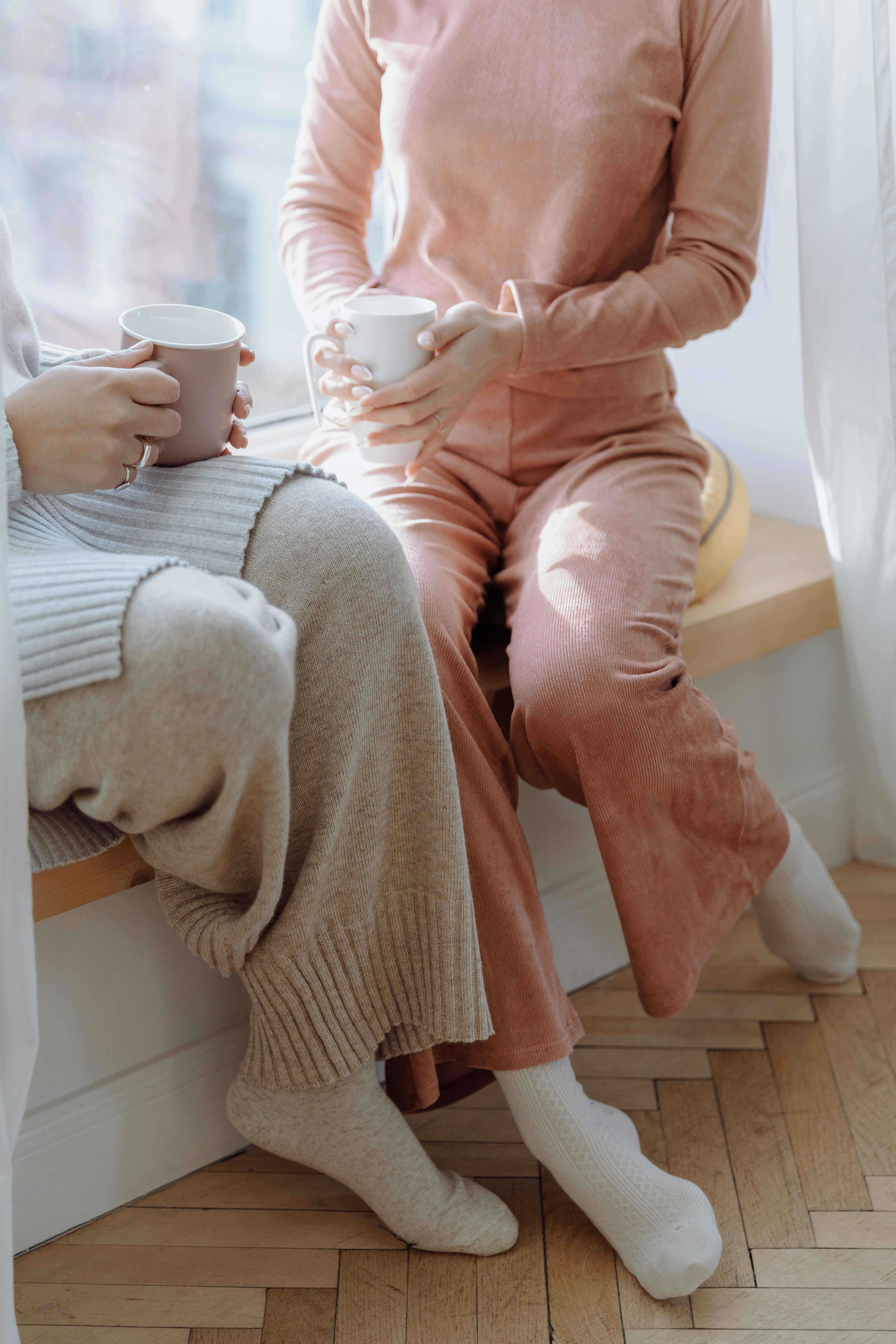 Two people enjoying coffee in loungewear by a sunny window.