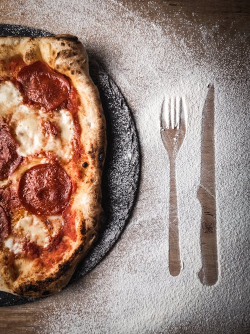 A Pizza and a Marked Knife and Fork by the Flour