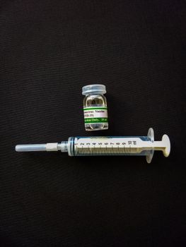 Syringe and COVID-19 vaccine vial on a black surface. Healthcare and medical concept.
