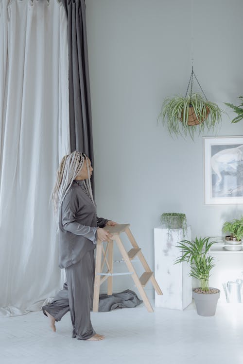 Free Woman in Gray Sleepwear Pajamas Holding a Wooden Step Stool Stock Photo