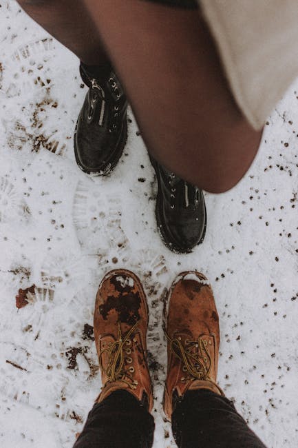 Top view of crop unrecognizable couple in outerwear and boots standing on snowy terrain in wintertime