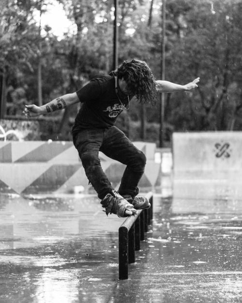 Free Skater doing a trick on a wet metal rail in a park in Mexico City. Black and white urban action shot. Stock Photo
