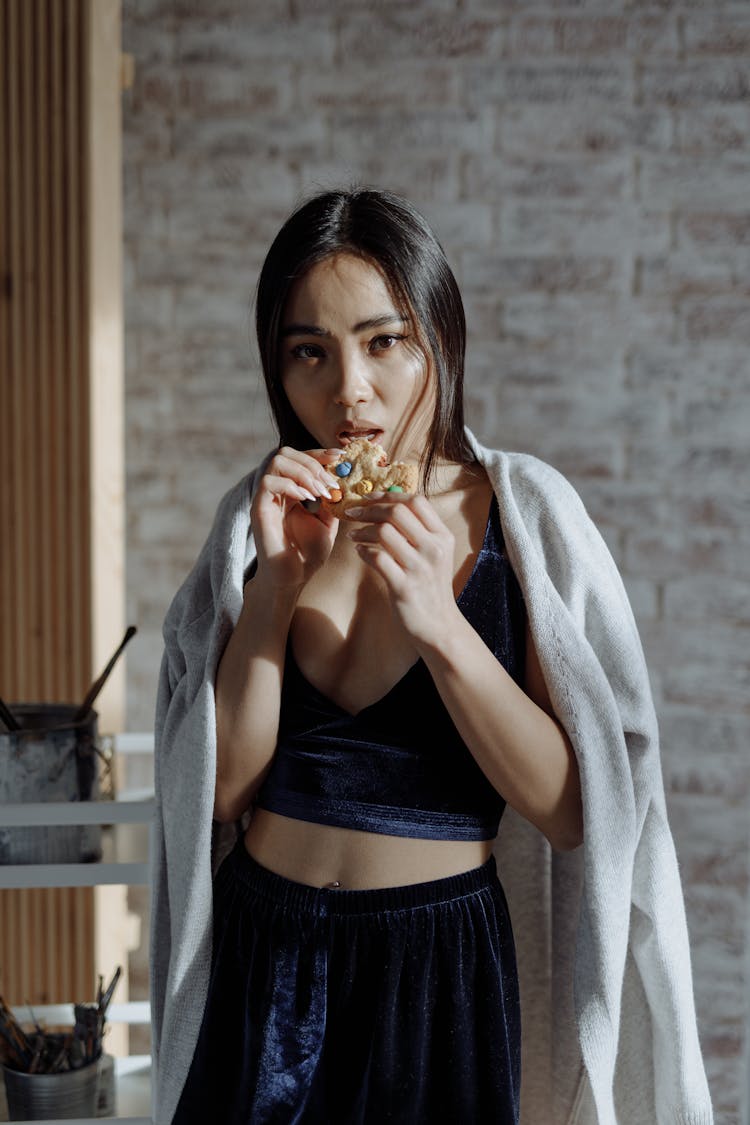 Woman Standing In Black Velvet Halter Crop Top Eating A Cookie