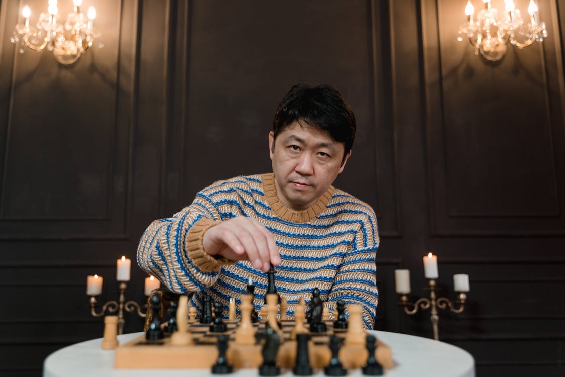 Man in Stripe Sweater Playing Chess Beside Black Wall