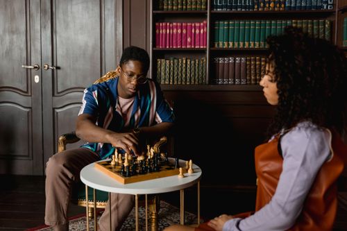 Free Two people playing chess in a warm, cozy library environment, focusing on strategy. Stock Photo