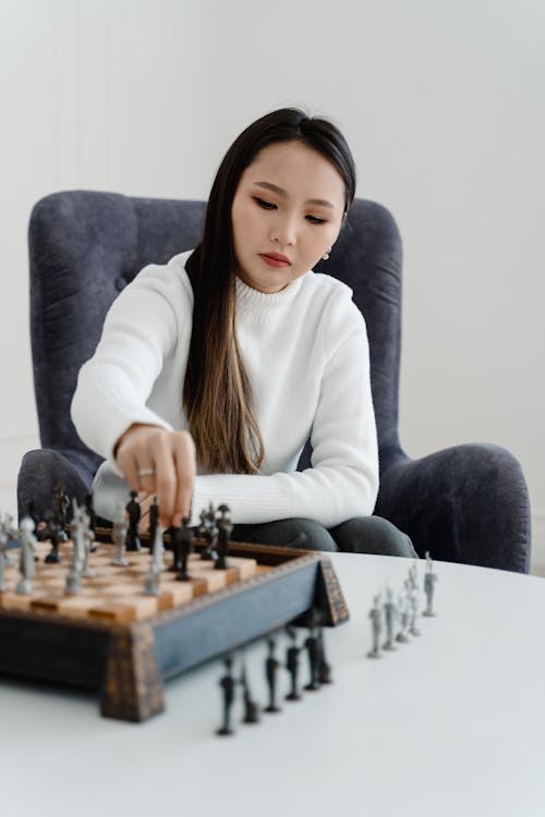 Pensive woman sitting at table in living room while thinking about next  chess move. Stock Photo by DC_Studio