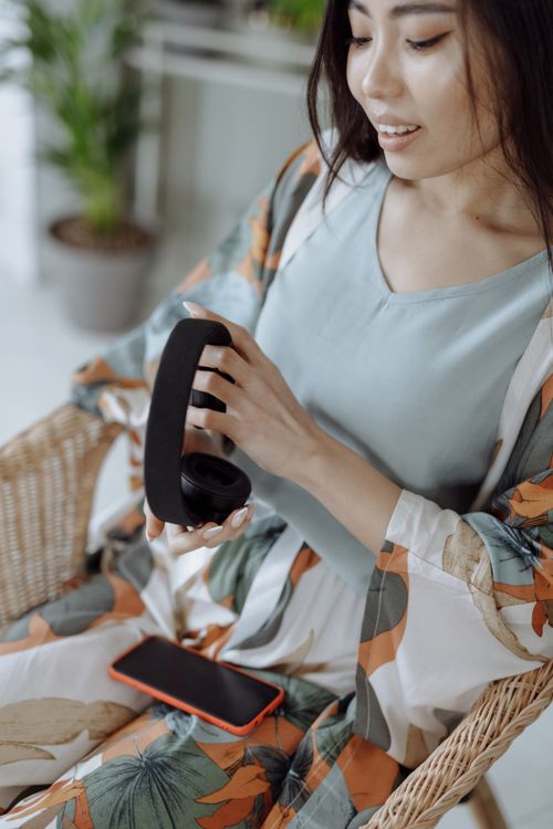 Free A young woman in floral pajamas holding headphones and smiling indoors, with a phone nearby. Stock Photo