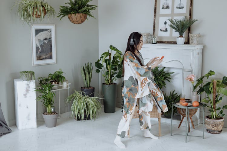 Woman In Floral Pajama Wearing Headphones And Dancing In The Room With Pot Plants