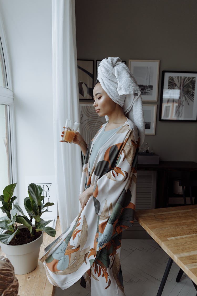 A Woman Standing Near The Window Holding A Drinking Glass