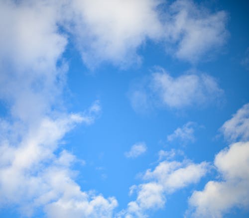 From below of abstract background of blue sky with floating white fluffy clouds in sunlight