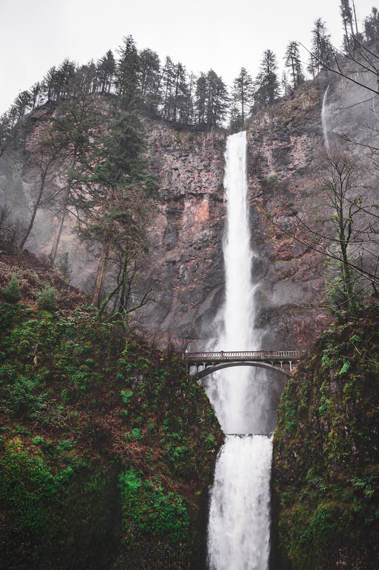 Wooden Bridge Over Picturesque Waterfall In Rocky Ravine