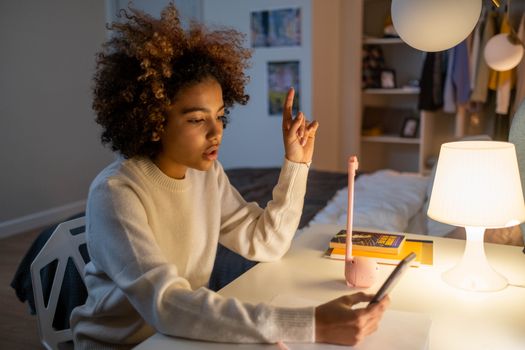 Teenager in white sweater using smartphone and gesturing during a videocall indoors.