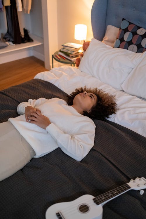 Free A Woman in White Sweater Lying on Bed Stock Photo