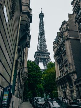 Street view of the Eiffel Tower framed by historic Parisian buildings, showcasing iconic architecture and city life.