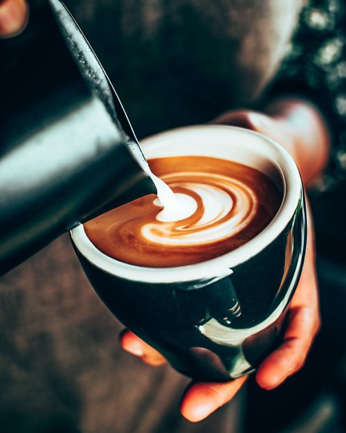 Free A barista skillfully pouring milk into a coffee cup, creating intricate latte art. Stock Photo