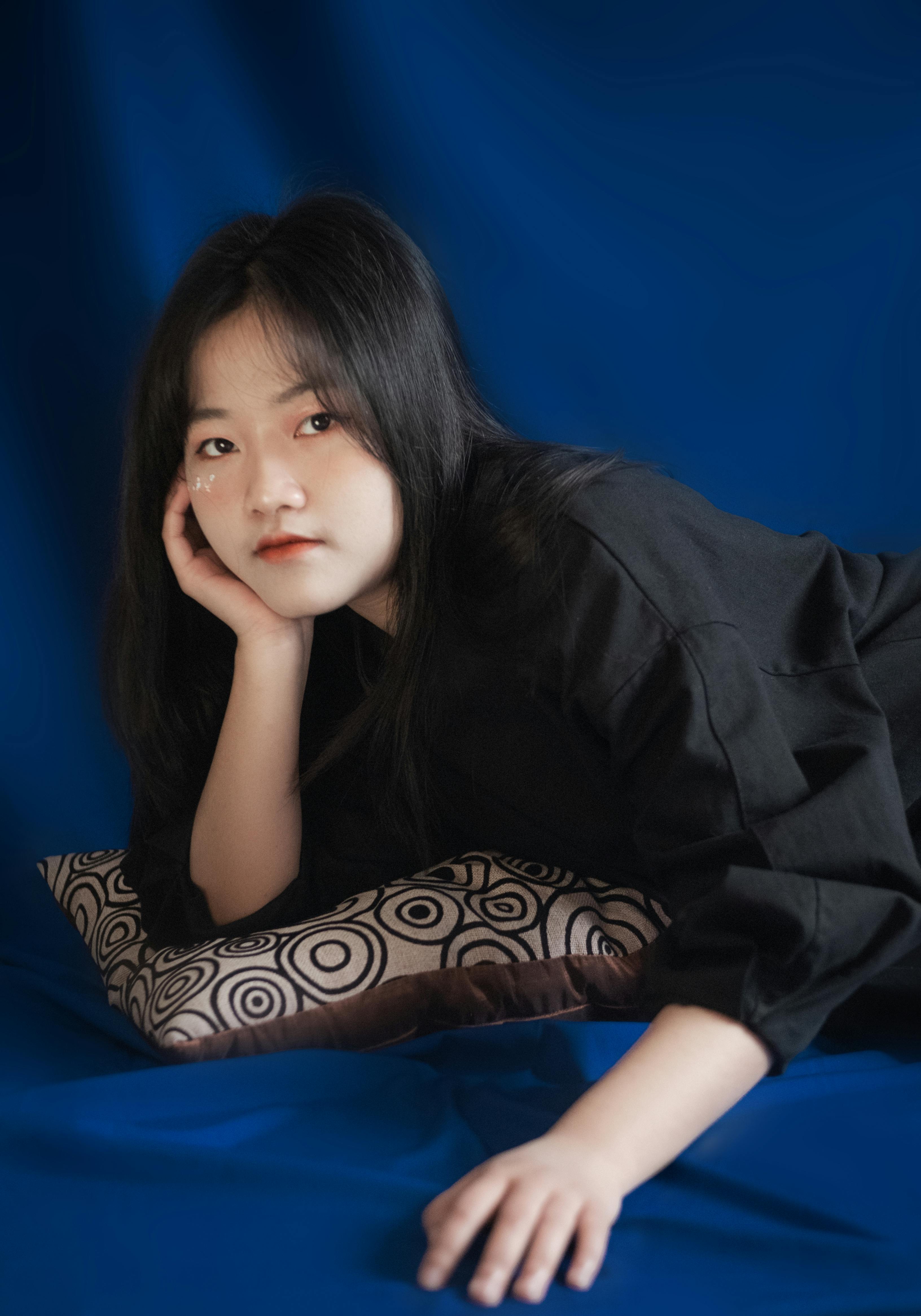 Elegant portrait of a young woman in black, posing thoughtfully against a blue backdrop.