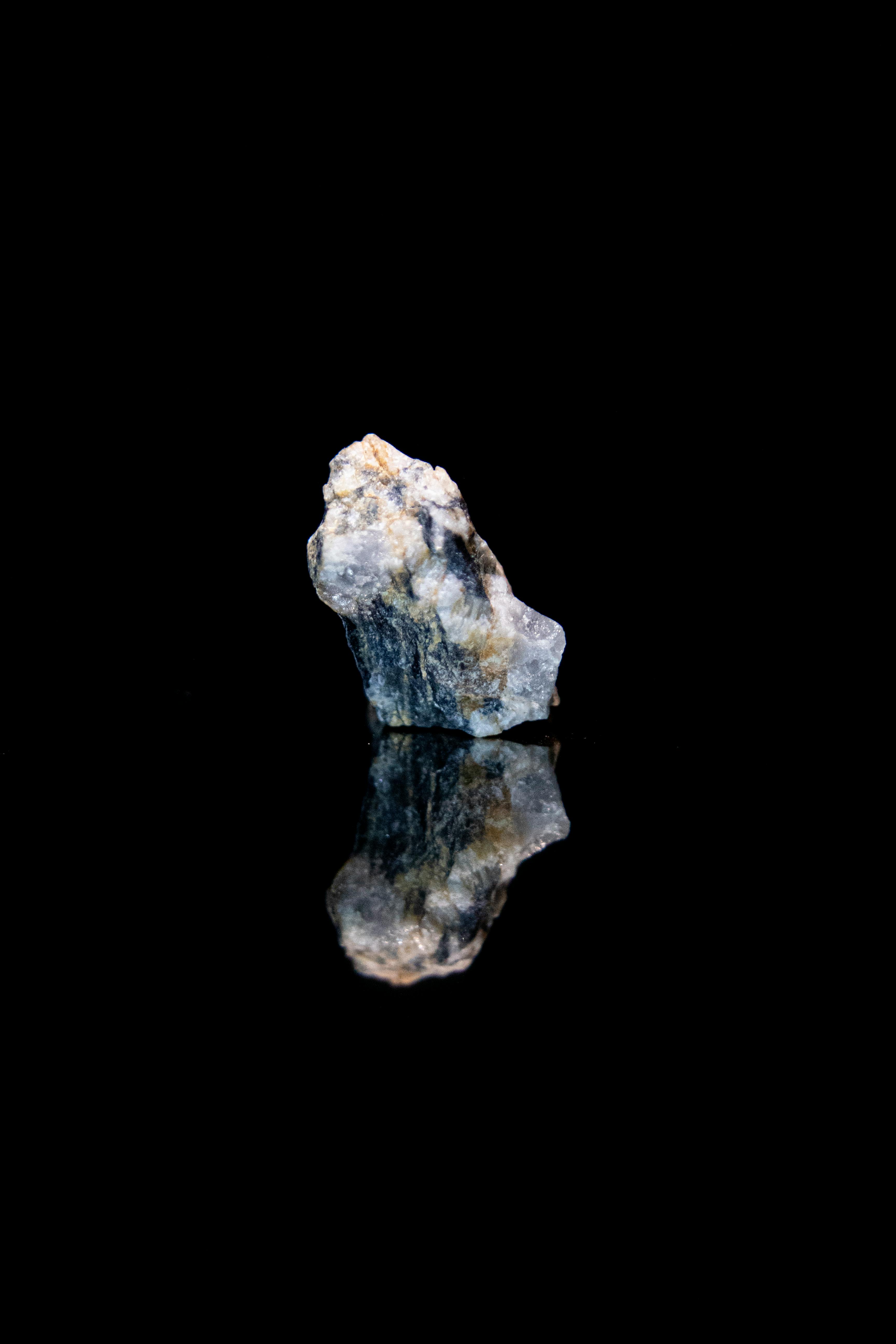 Raw mineral specimen on shiny black reflective surface showing iridescent color play and natural texture