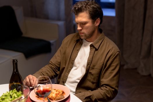 Man seated at dinner table with wine, lasagna, and salad, appearing thoughtful.