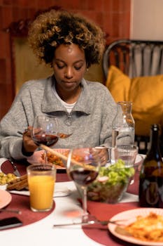 Woman enjoying dinner with wine at a cozy home setting. Indoors, warm ambiance.