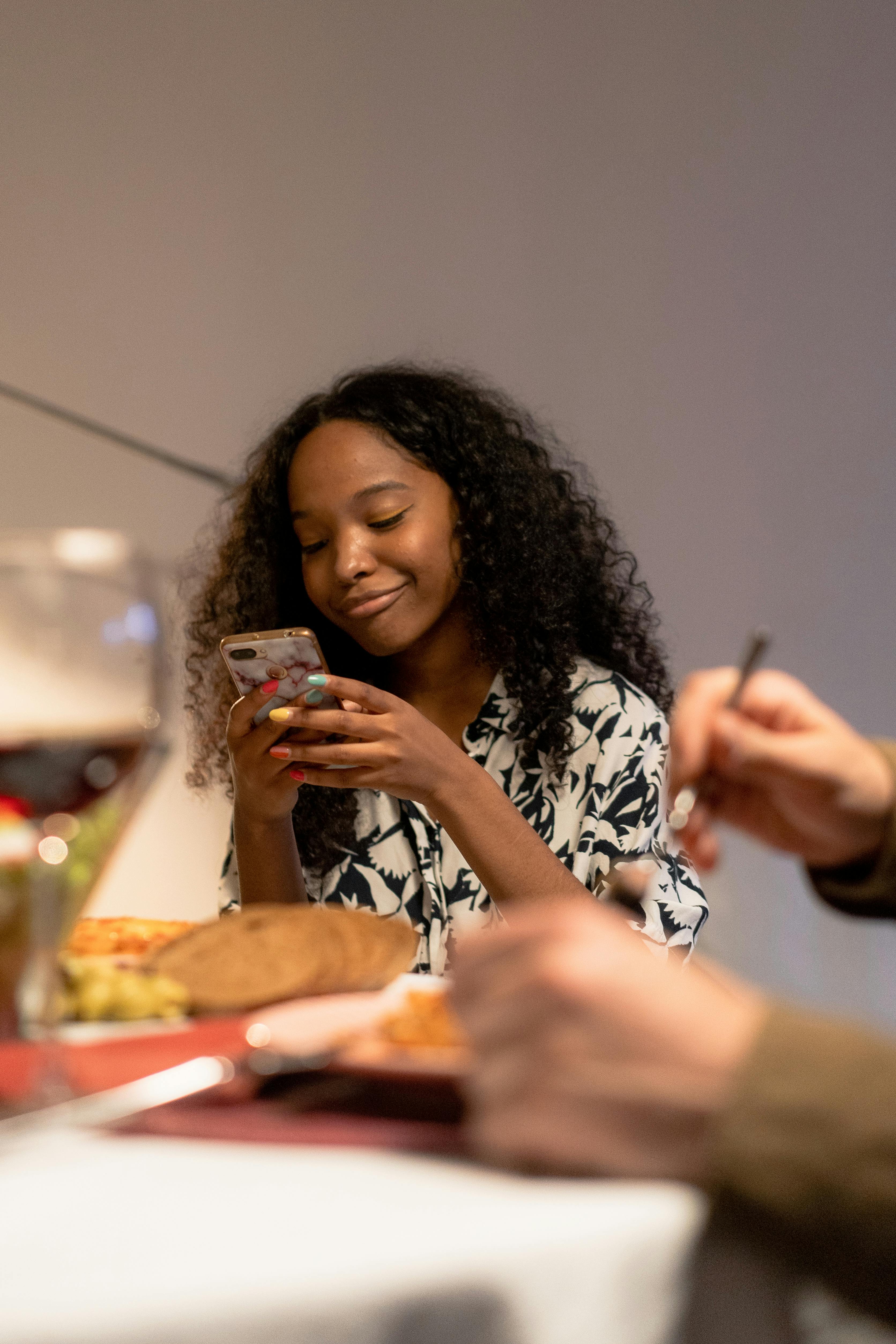 smiling young girl sitting in printed blouse holding smartphone in front of dining table