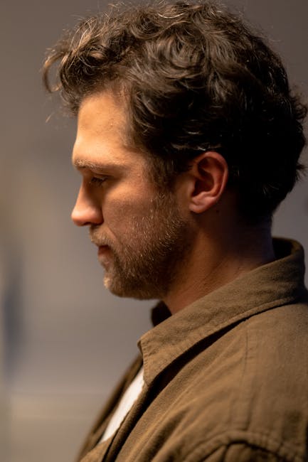 Side profile portrait of a man with facial hair in a brown shirt, looking contemplative.