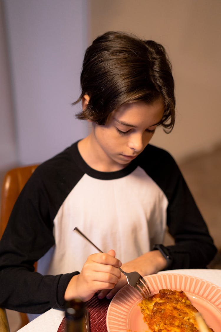 Boy In White And Black Shirt Eating Lasagna