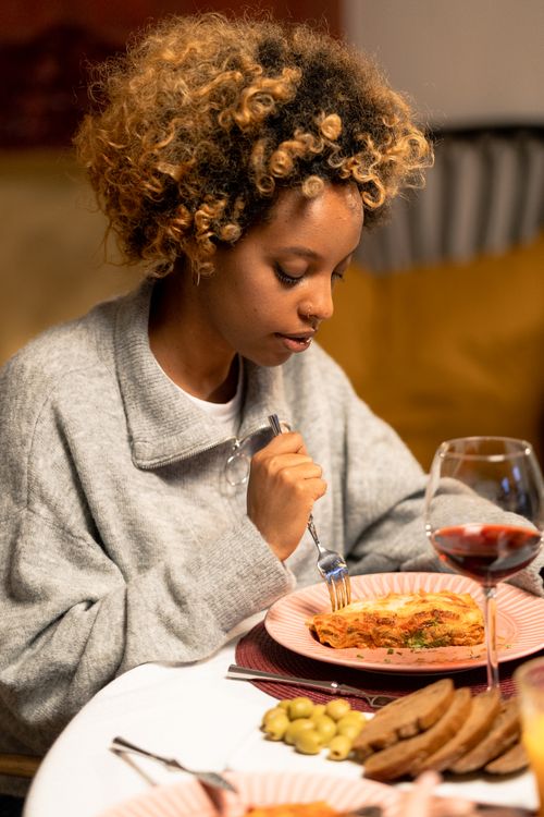 Free African American woman enjoying a cozy meal with wine and pasta at home. Stock Photo