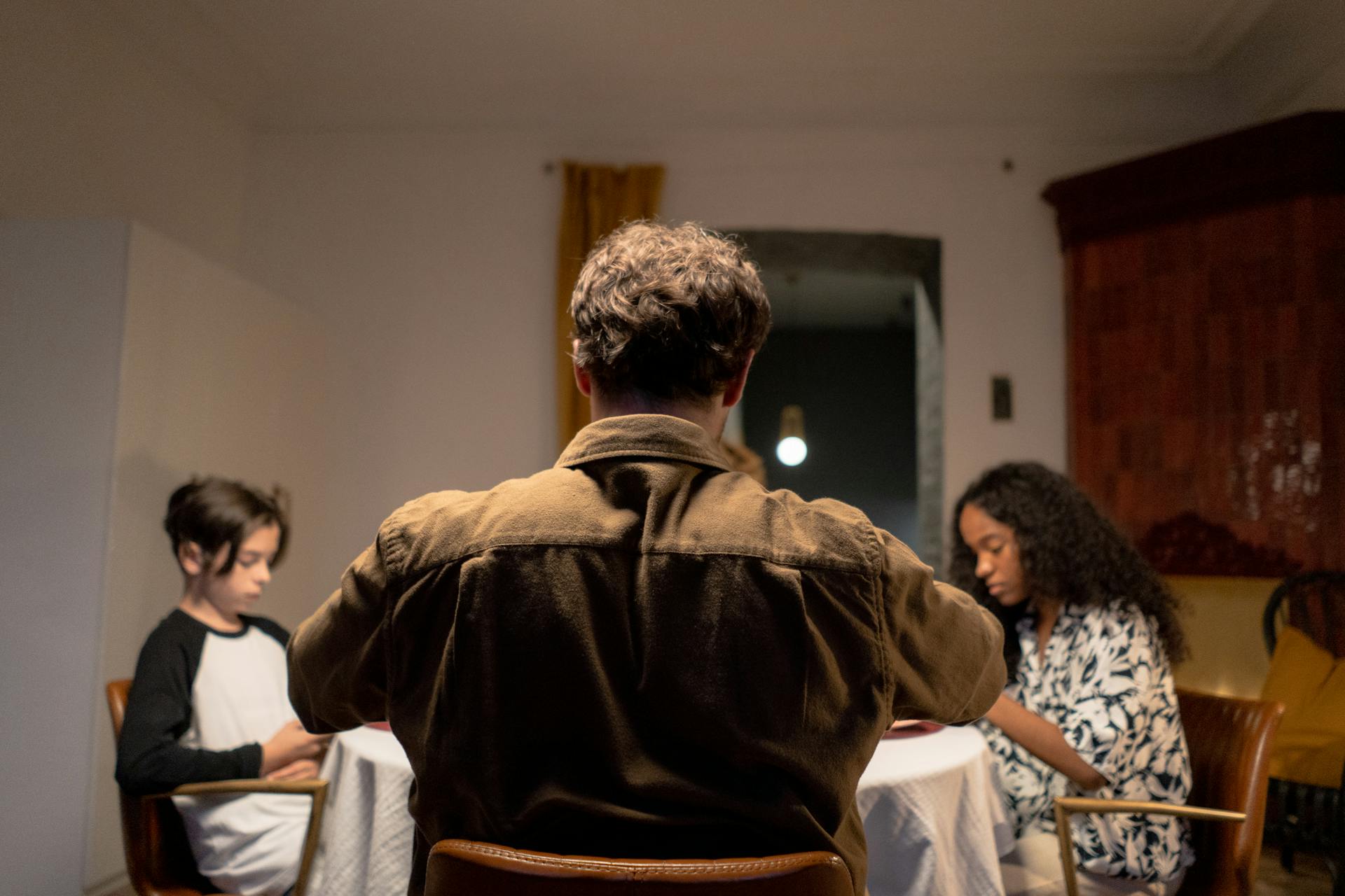 A family gathers around a dining table, featuring a father and two children in an intimate setting.