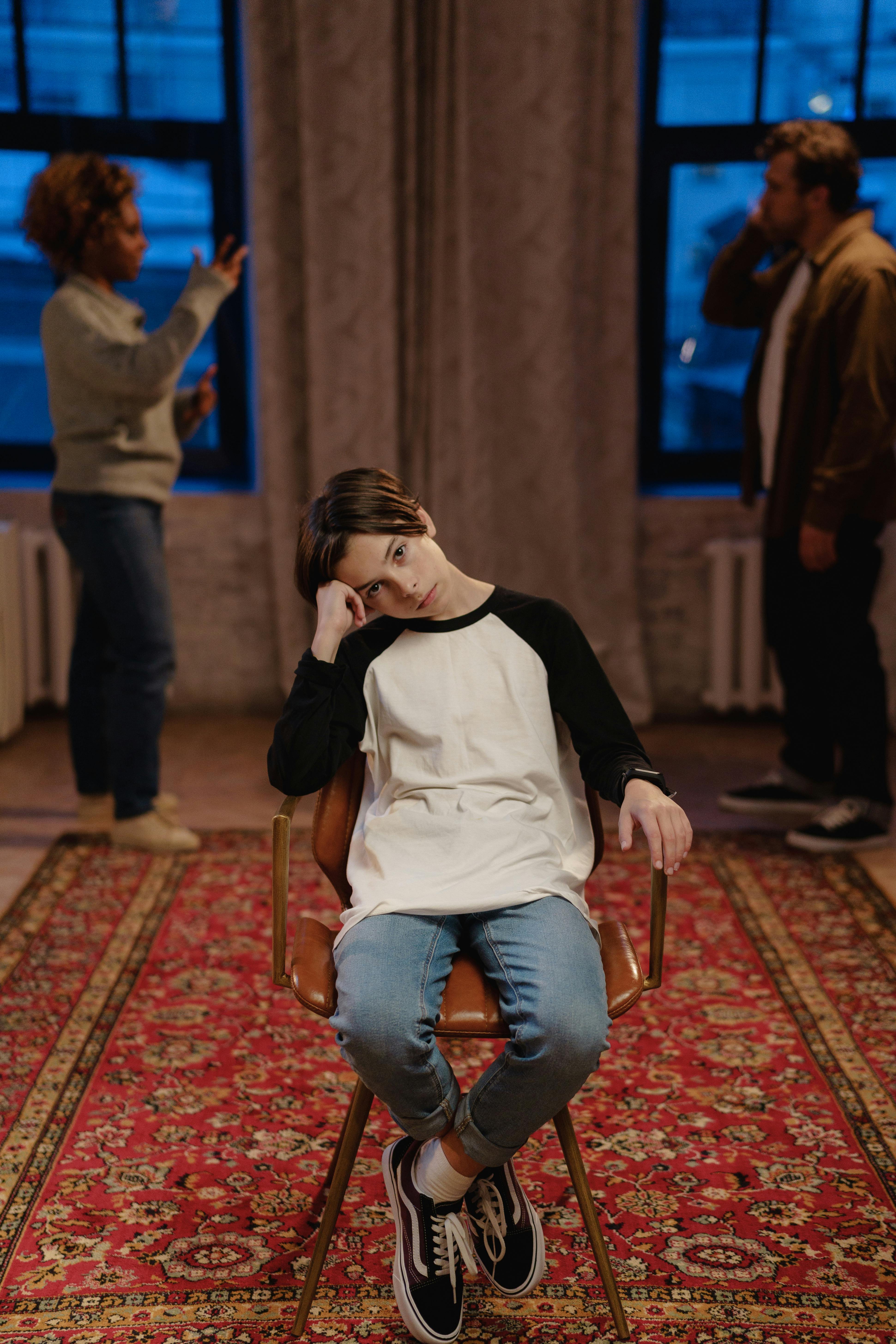 a boy sitting on a chair with quarreling parents behind