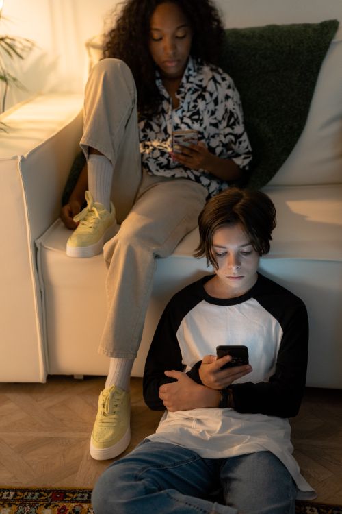 Free A black girl and caucasian boy using smartphones in a cozy living room setting. Stock Photo