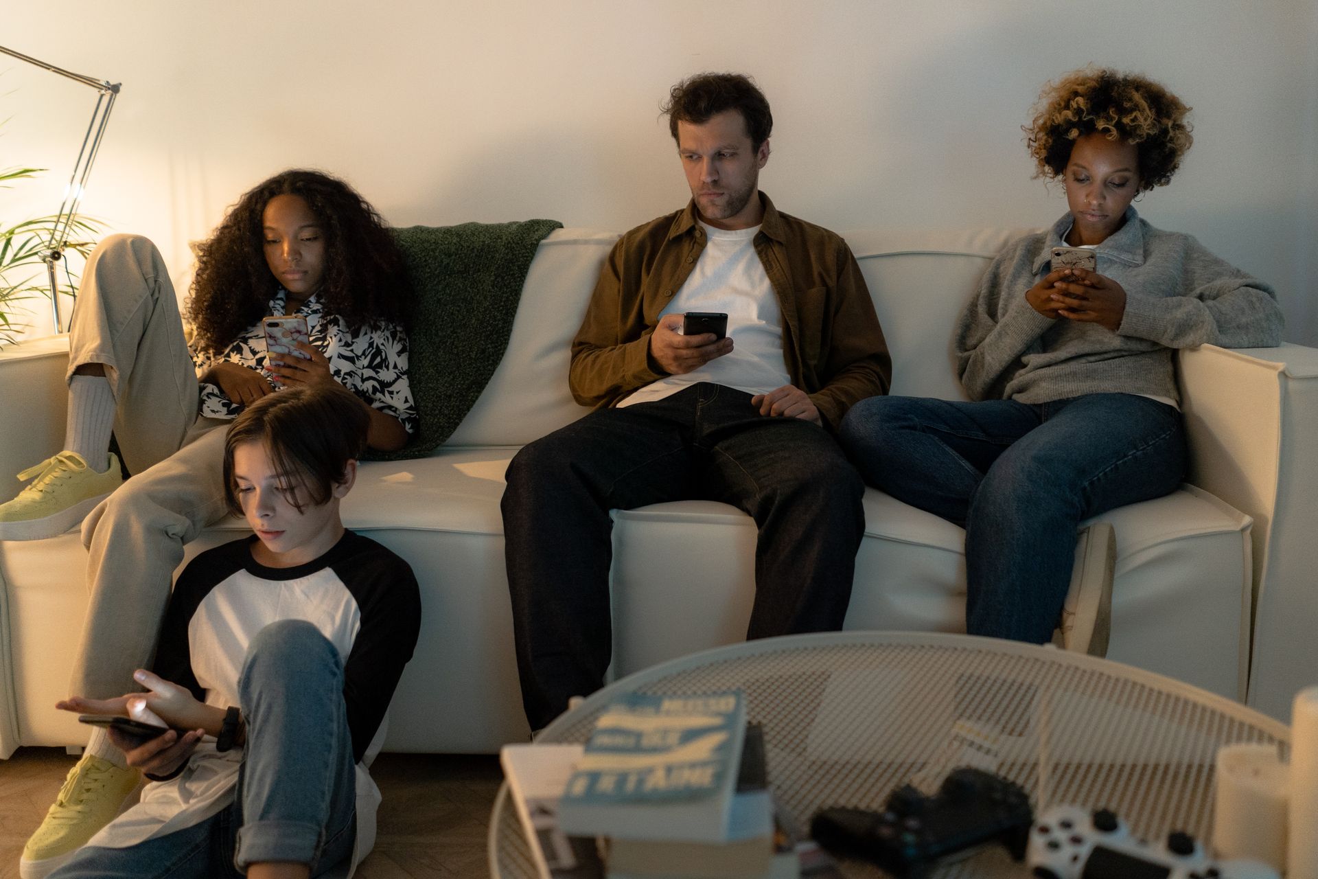 A diverse family sits on a sofa using their smartphones together indoors.