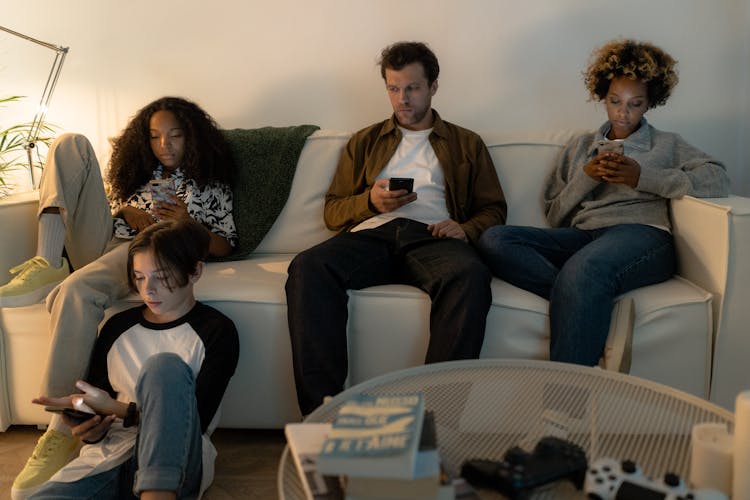 A Family Sitting On Sofa Holding Cellphones