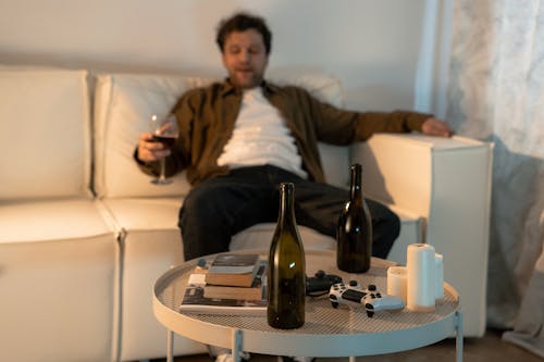 Free Man Sitting on White Sofa with Glass of Wine Beside Table with Bottles and Candles Stock Photo