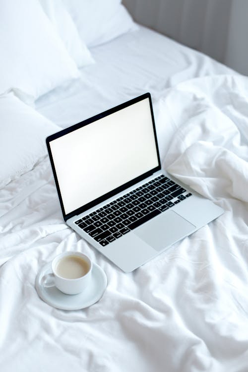Free A Silver Laptop Beside a Cup of Coffee on Bed Stock Photo