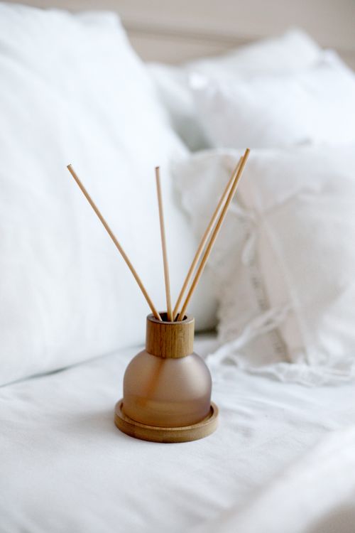Free Elegant reed diffuser with wooden sticks on a bed of white linen for a serene home ambiance. Stock Photo