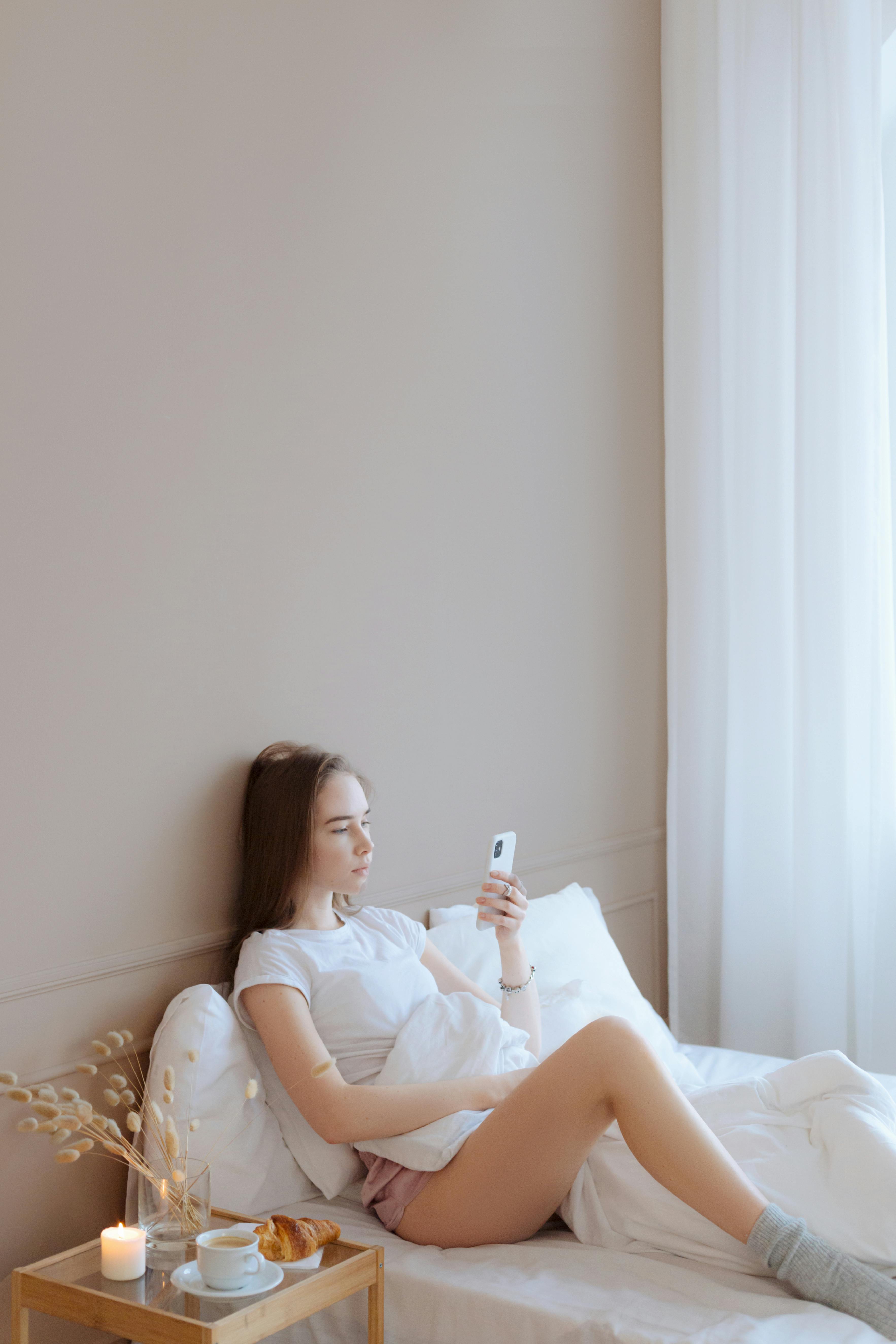 a woman sitting on bed holding a cellphone