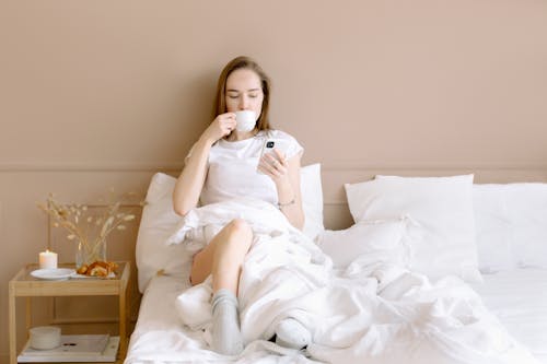 Free Woman Drinking from a Mug While Sitting on the Bed Stock Photo
