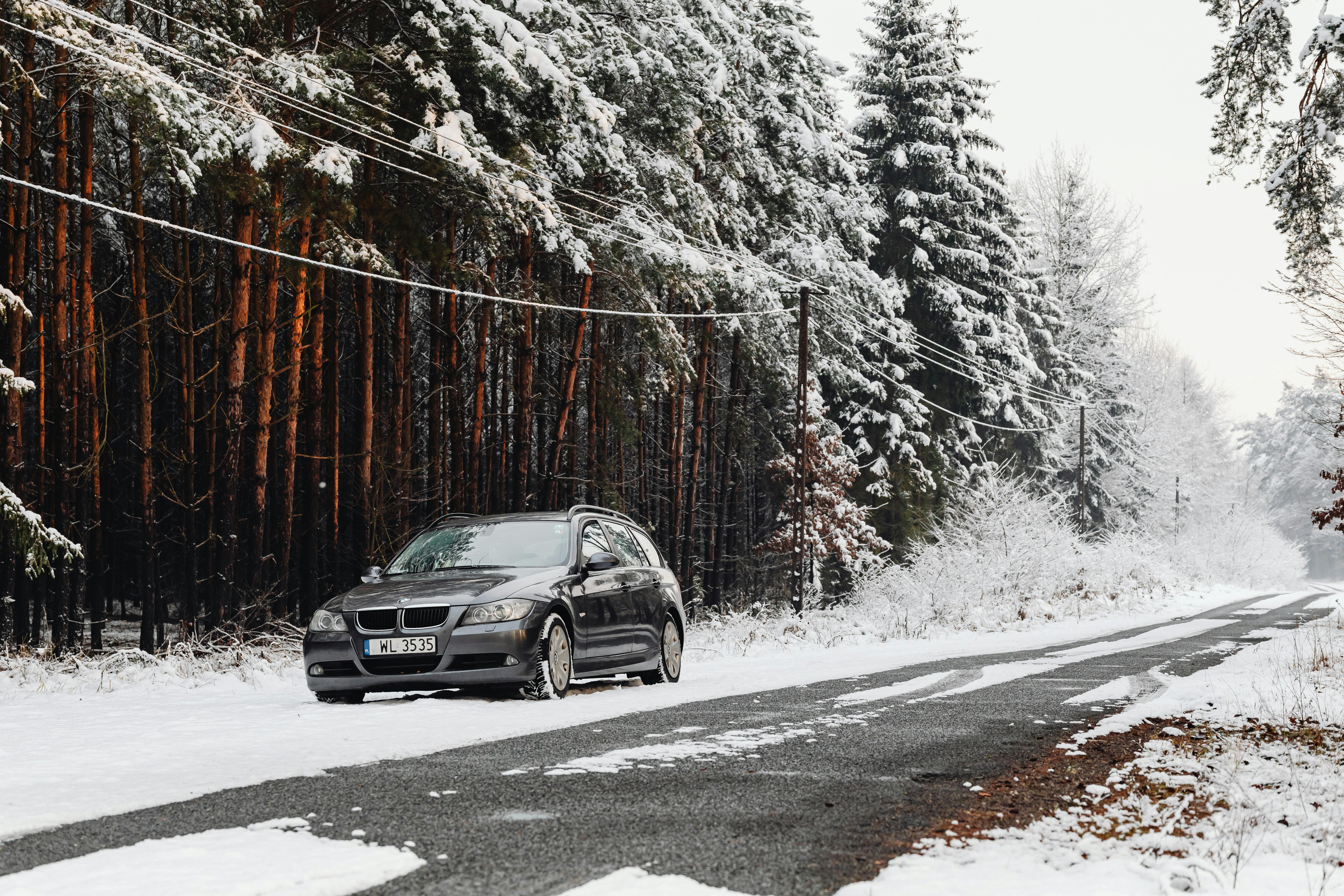 Car parked on a snow-covered road beside a winter forest landscape, ideal for travel themes.